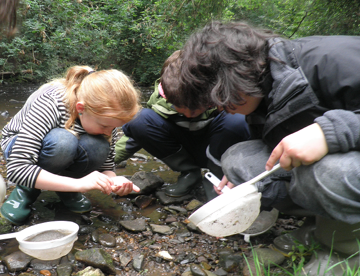 3 children crouch on the river bank to look at what they caught in their sieves from the river
